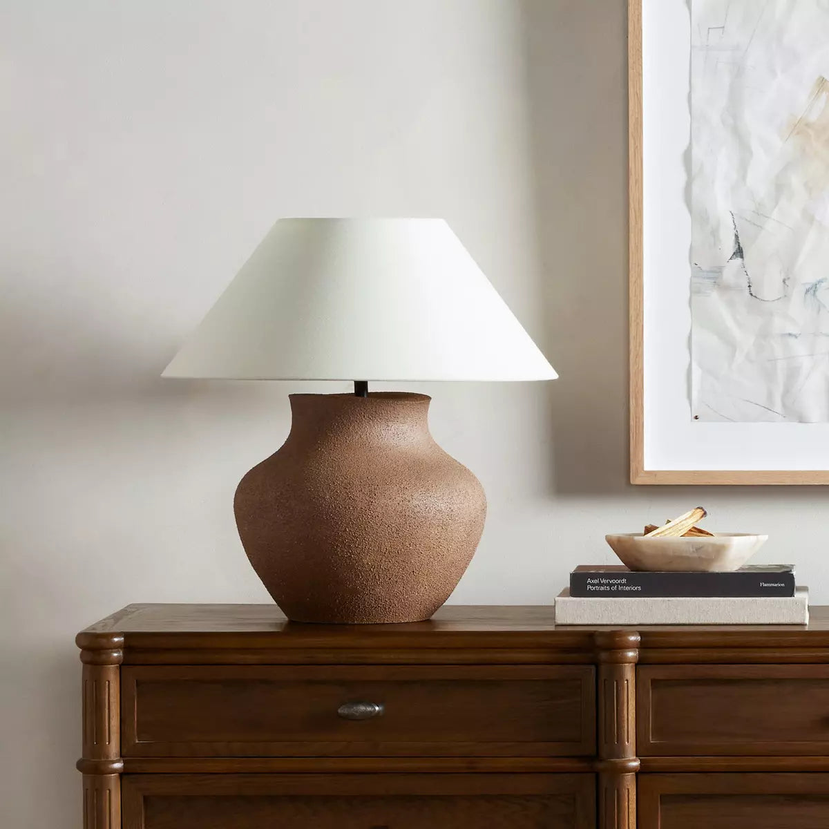 This table lamp is crafted in the shape of a classic vase, this ceramic lamp boasts a rich, textured sand coating that adds a touch of natural charm. It comes with a tapered linen shade in a versatile ivory hue for a sophisticated finish.