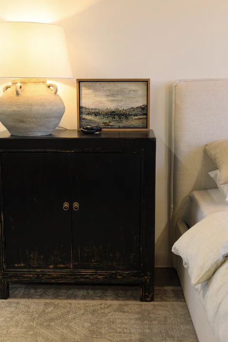 Cozy bedroom featuring a cream upholstered bed, black vintage nightstand, and ambient lighting creating a warm, soft-hued atmosphere